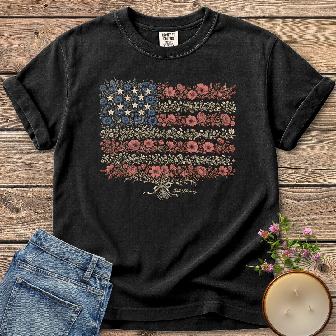 Still Blooming t-shirt, an American flag made of wildflowers with Still Blooming in script, on a Black Comfort Colors tee