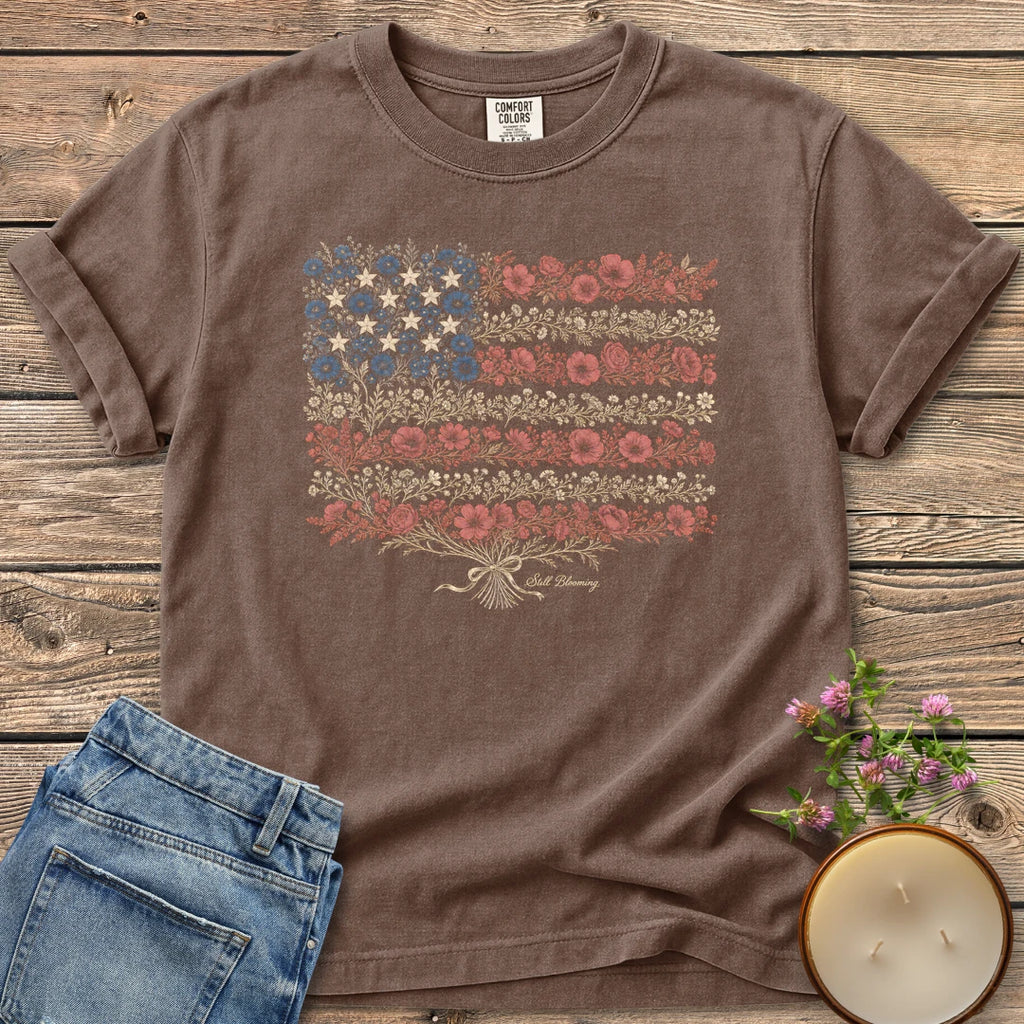 Still Blooming t-shirt, an American flag made of wildflowers with Still Blooming in script, on an Espresso Comfort Colors tee
