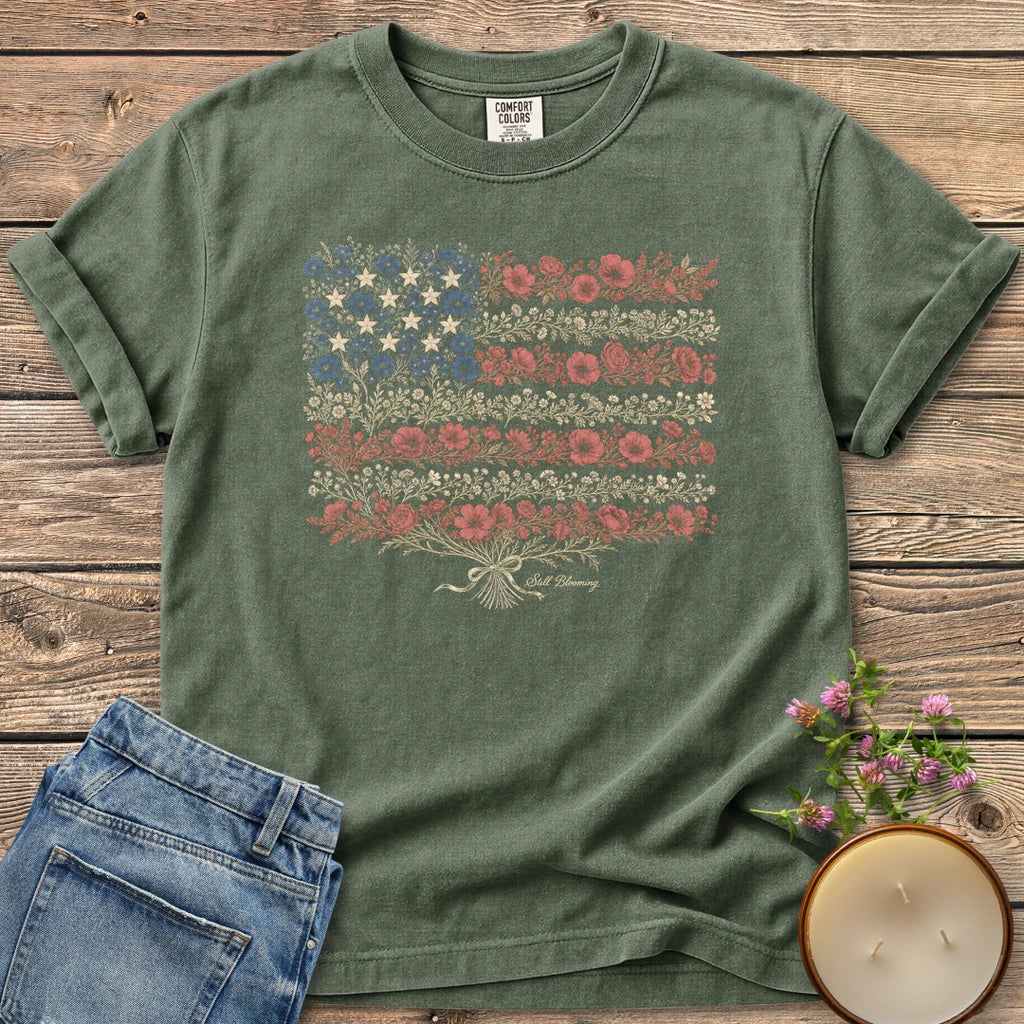 Still Blooming t-shirt, an American flag made of wildflowers with Still Blooming in script, on a Moss Comfort Colors tee