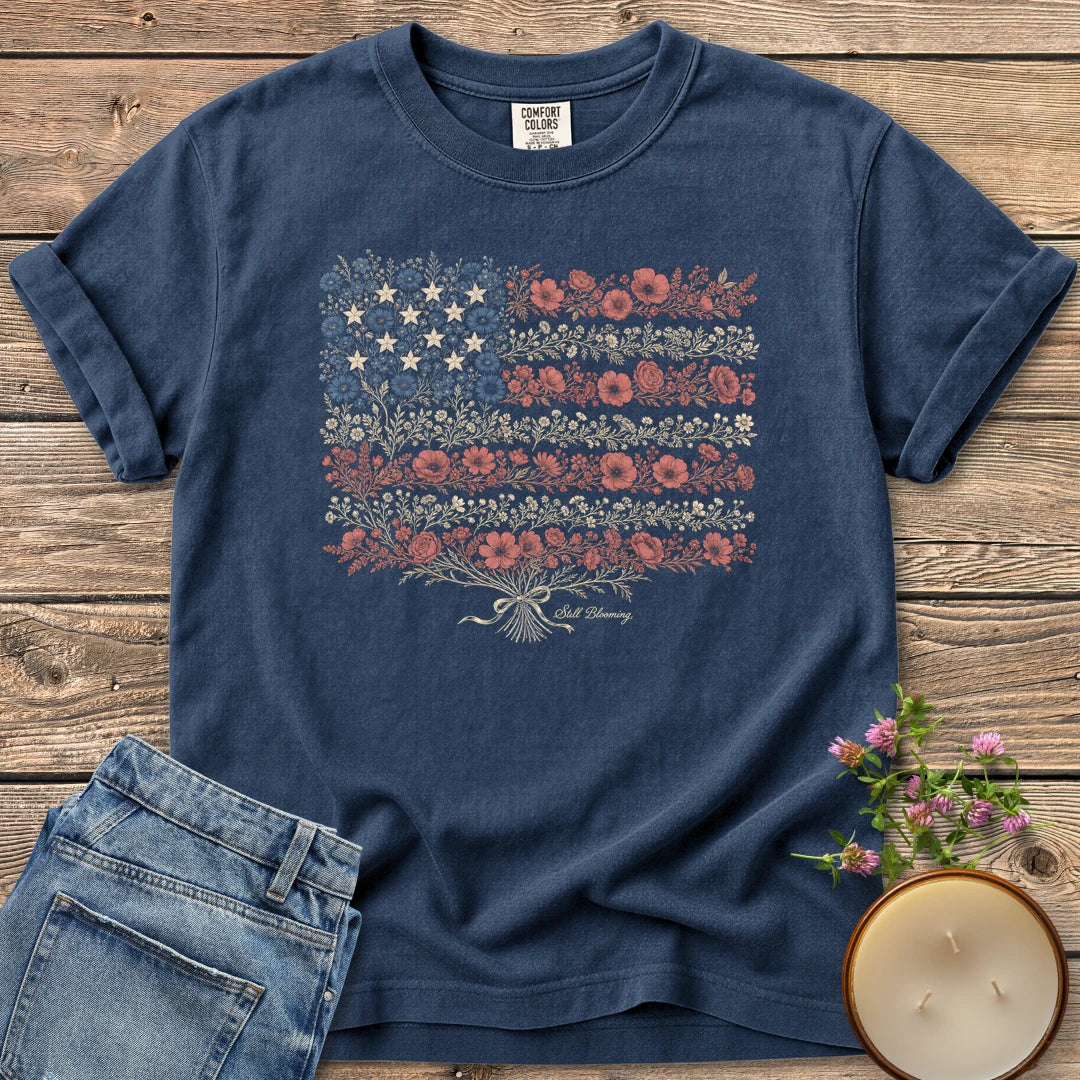 Still Blooming t-shirt, an American flag made of wildflowers with Still Blooming in script, on a Navy Comfort Colors tee