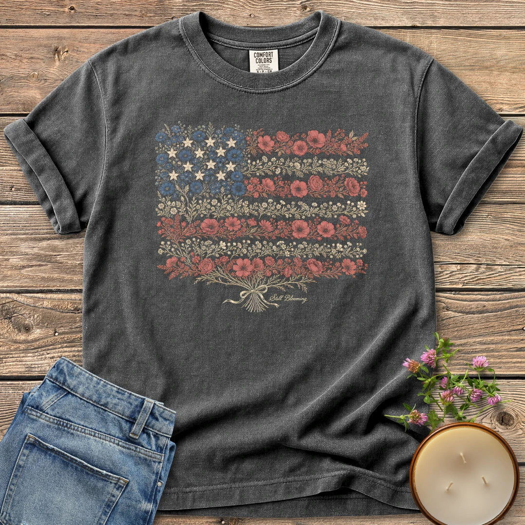 Still Blooming t-shirt, an American flag made of wildflowers with Still Blooming in script, on a Pepper Comfort Colors tee
