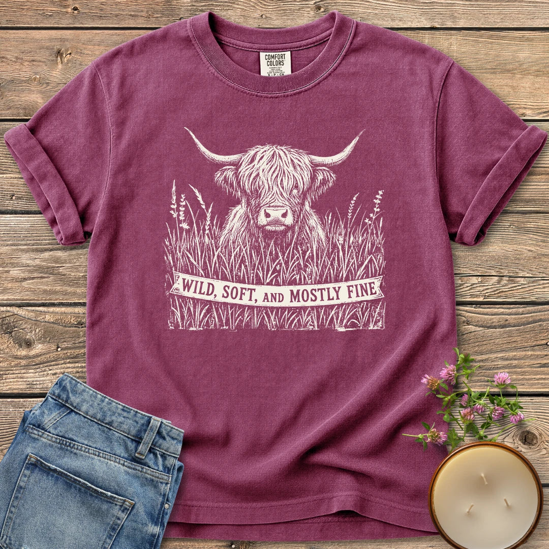 Wild Soft And Mostly Fine t-shirt, a shaggy highland cow in tall grass with a banner reading Wild, Soft, and Mostly Fine, on a Berry Comfort Colors tee