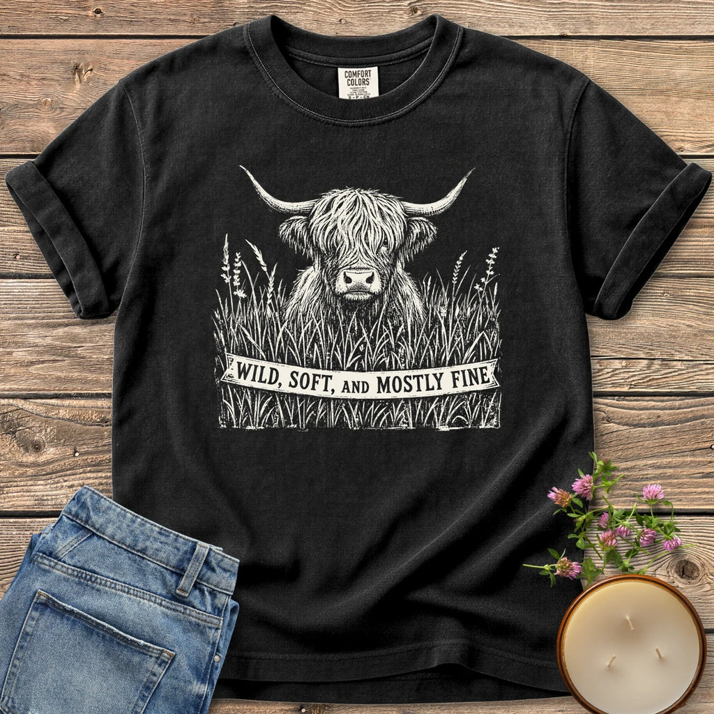 Wild Soft And Mostly Fine t-shirt, a shaggy highland cow in tall grass with a banner reading Wild, Soft, and Mostly Fine, on a Black Comfort Colors tee