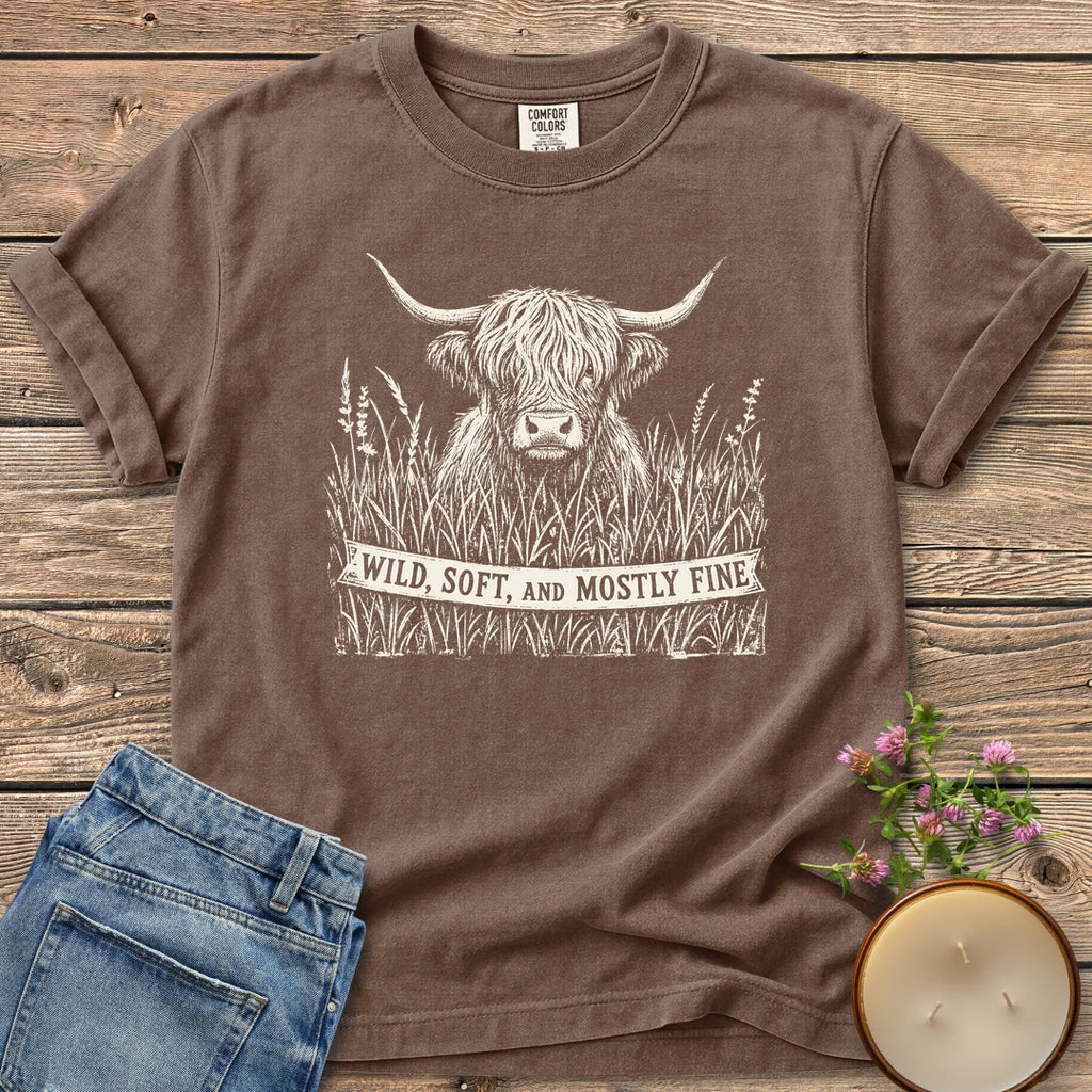 Wild Soft And Mostly Fine t-shirt, a shaggy highland cow in tall grass with a banner reading Wild, Soft, and Mostly Fine, on an Espresso Comfort Colors tee