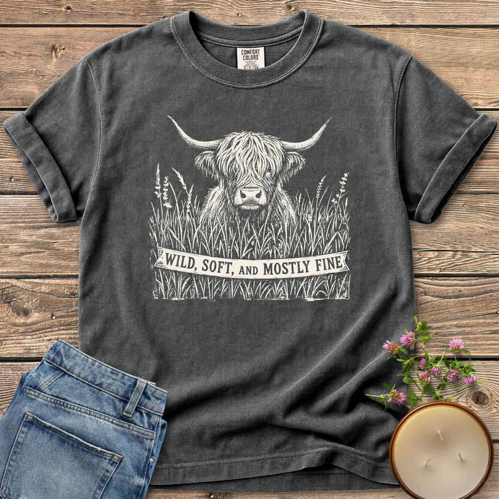 Wild Soft And Mostly Fine t-shirt, a shaggy highland cow in tall grass with a banner reading Wild, Soft, and Mostly Fine, on a Pepper Comfort Colors tee
