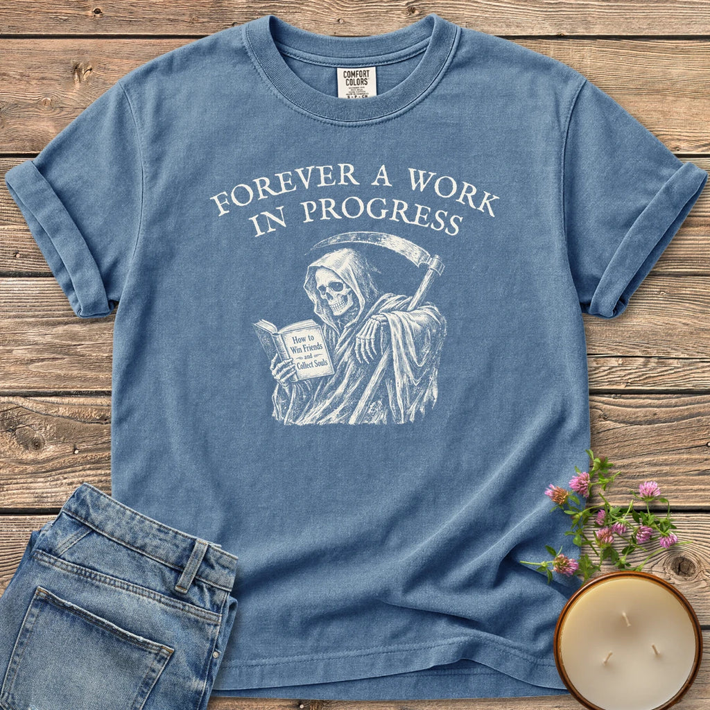 Win Friends Collect Souls t-shirt, a grim reaper reading How to Win Friends and Collect Souls under Forever A Work In Progress, on a Blue Jean Comfort Colors tee